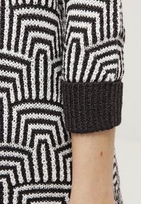 Svetr pletený v černobílém pruhu s geometrickým vzorem a žebrovanými černými manžetami. Měkká textura s těsným střihem na zápěstích.