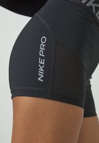 Black Nike Pro shorts feature a fitted design, smooth texture, and side mesh panel. The brand name is displayed in gray on the thigh.