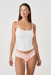 Débardeur en dentelle blanche avec de fines bretelles et une taille en dentelle rose sur des sous-vêtements taille haute. Tissu doux et texturé.
