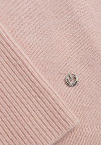 Pull en tricot rose clair avec des poignets côtelés, arborant un logo en forme de cœur argenté. Texture douce et détails de design minimalistes.