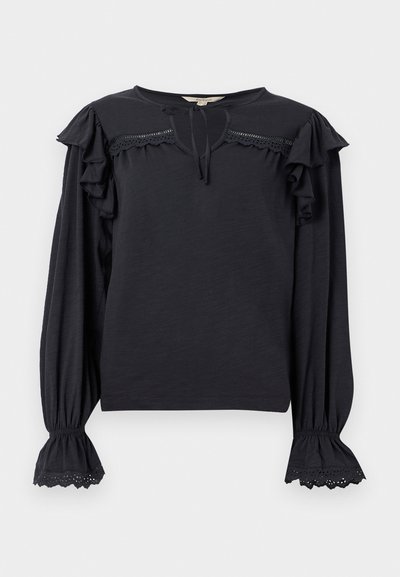 Blouse noire à manches longues avec épaules à volants, bordure en dentelle sur la poitrine et les poignets, bracelets élastiqués et encolure goutte avec lien.