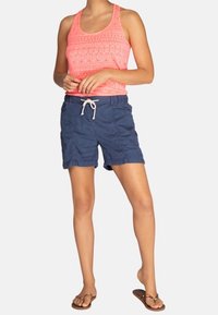 Top de tirantes de estampado rosa brillante, pantalones cortos de cuerda navy azul, chanclas. El top presenta un diseño texturizado, los pantalones cortos tienen un corte relajado.