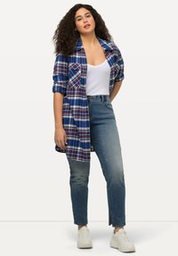 Kostkovaná flanelová košile v modré a červené barvě přes bílý tílko, doplněná o světle modré džíny a bílé tenisky. Má dlouhé rukávy a kapsy.