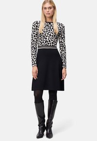 Czarna sukienka z dopasowanym topem w leopardzie wzory, z długimi rękawami. Prezentuje elegancki sylwetkę, uzupełnioną czarnymi wysokimi kozakami.