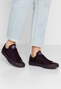 Svarta canvas låga sneakers med runda tån, glänsande tåskydd och platta snören. Bärs med ljusblå, korta jeans med fransiga fållar.