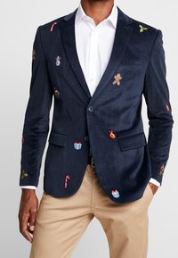 Granatowy żakiet z korduroyu z kolorowym haftem w tematyce świątecznej, w tym cukrowe laski, pierniczki i prezenty.