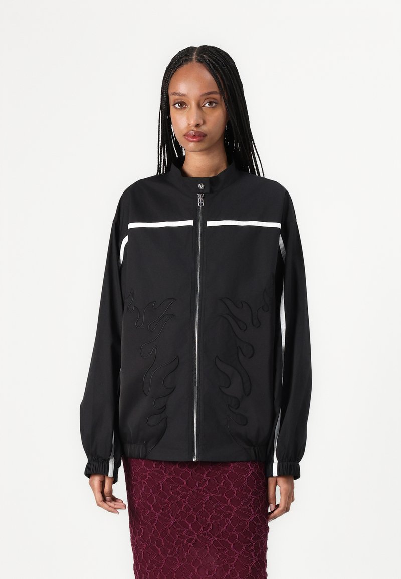 Black bomber jacket with flame embroidery, a zip front, and white stripes on shoulders. Features elastic cuffs and a standing collar.