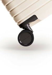 Harde koffer in crèmekleur met verticale groeven. Voorzien van een zwarte wiel met een gestructureerd oppervlak en brandingdetail, wat de stabiliteit verbetert.