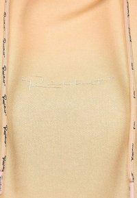 Top ribbed beige chiaro con zip frontale, caratterizzato da un logo ricamato bianco e cuciture nere a contrasto lungo i bordi della zip.