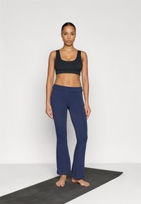 Čierna športová podprsenka so širokými ramienkami v kombinácii s tmavomodrými rozšírenými jogovými nohavicami. Materiál pôsobí pružne, s hladkou textúrou a priliehavým strihom.