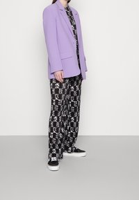 Blazer oversize in lavanda, pantaloni larghi a fantasia bianco e nero, e sneakers nere. Tessuto liscio e vestibilità comoda.