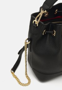 Sac seau en cuir noir avec quincaillerie en métal doré, une surface texturée et une bandoulière en chaîne amovible. Intérieur doublé de rouge.