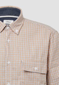 Geruit overhemd in beige en wit met een button-down kraag, twee voorzakken en een zachte textuur. Beschikt over kleine witte knopen.