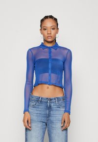 Sheer blue mesh long-sleeve shirt with a collar and button-down front, cropped cut, paired with light blue denim jeans.