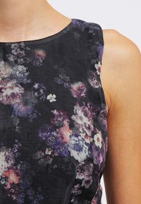 Blommig ärmlös topp med svart botten och flerfärgade blommönster, strukturerad tyg och rund halsringning.