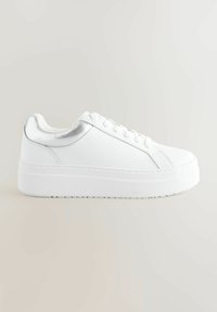 Sneaker bianco con collo imbottito e accento argentato metallico. Presenta una suola in gomma spessa e rialzata e lacci piatti. Texture liscia.