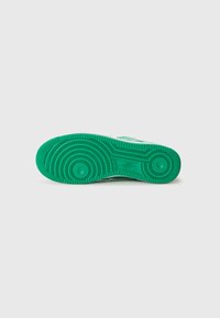 Green rubber sneaker sole with circular treads, textured surface, and embossed logo. Flat design with rounded edges and ridged patterns.