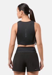 Top corto deportivo negro con una textura suave, que presenta un logo en la parte posterior. Combinado con pantalones cortos negros de corte holgado y cintura elástica.