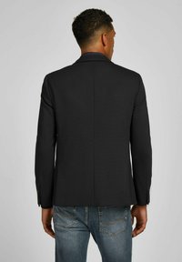 Zwarte blazer met een getailleerde pasvorm, gladde stof, scherpe revers en enkele achterzoom. Gecombineerd met blauwe denim jeans voor een casual uitstraling.