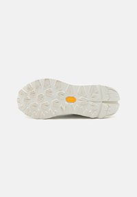 Semelle en caoutchouc blanc avec un motif texturé et robuste. Comprend un accent logo jaune, conçu pour l'adhérence et la durabilité dans des conditions extérieures.