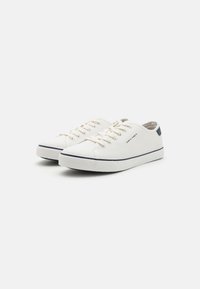 Zapatillas de lona blancas con cierre de cordones, suela de goma, acento en azul marino en el talón y raya azul marino en contraste a lo largo de la entresuela.