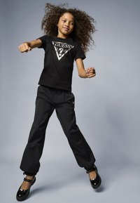 Black cotton t-shirt with silver triangle logo, black nylon pants, and shiny black shoes. Model depicted in a dynamic pose.