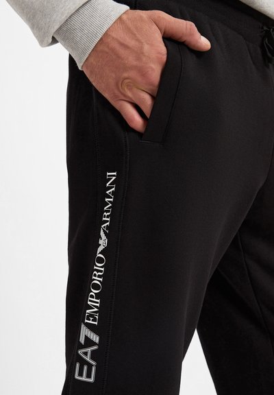 Pantaloni sportivi neri in misto cotone con vita elastica, tasche laterali e marchio bianco "EA7 Emporio Armani" lungo la gamba.