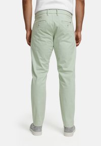 Light green cotton chinos with two back pockets, a smooth texture, and a slim fit. Worn with gray slip-on shoes.