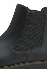 Stivale alla caviglia in pelle nera con pannello laterale elastico, finitura testurizzata e suola robusta. I dettagli delle cuciture aggiungono un sottile interesse nel design.