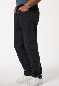 Vaqueros de denim oscuro con un corte ajustado, con costuras texturizadas y bolsillos laterales, combinados con zapatillas blancas.