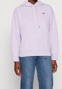 Felpa lavanda in misto cotone con cappuccio regolabile, tasca a marsupio e logo rosso Levi's. Vestibilità comoda con polsini e fondo a costine.