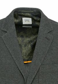 Blazer gris foncé texturé avec des revers crantés, une doublure intérieure à motif floral et une étiquette de la marque Camel Active à l'intérieur du col.