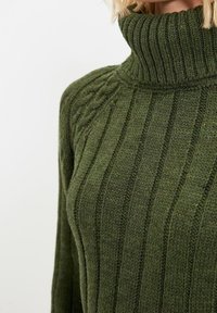 Grüner Rippstrickpullover mit hohem Rollkragen und strukturierten Details an den Schultern. Weicher, mitteldicker Stoff mit vertikalen Linien.