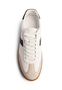 Sneaker bianca con punta in suede beige, striscia laterale nera, lacci bianchi e suola in gomma color caramello, vista dall'alto su sfondo bianco.