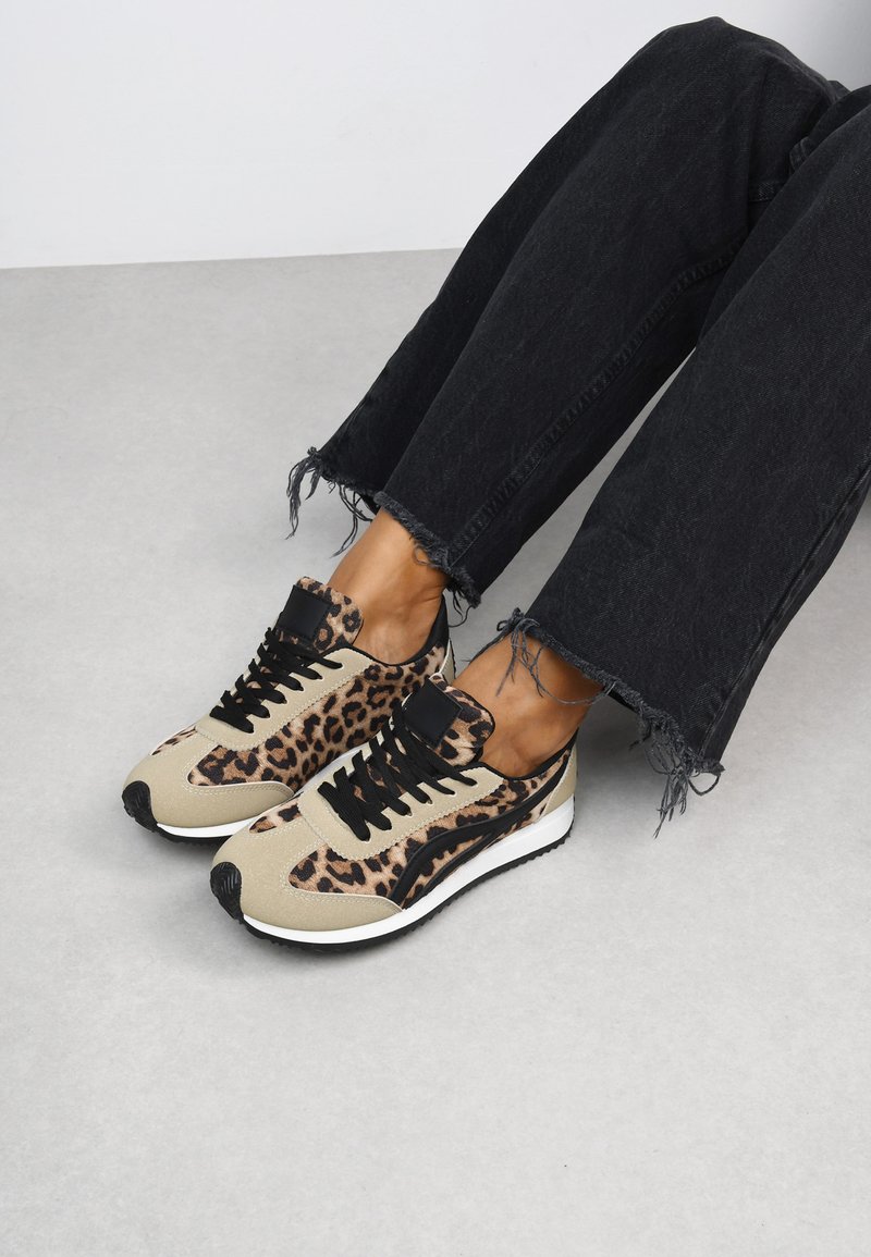 Sneakers con stampa leopardata marrone e nera con superficie texturizzata, lacci neri e suola bianca; indossati con jeans neri sfrangiati.