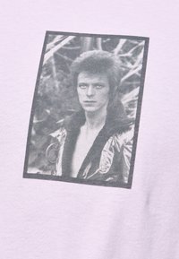 Světle fialové tričko s vintage černobílým obrázkem osoby v metalické bundě, zarámované v černé.