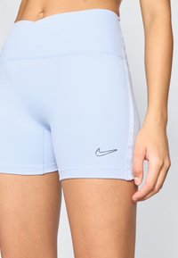 Ανοιχτό μπλε αθλητικές βερμούδες με λεία υφή, υψηλή μέση και μαύρο λογότυπο Nike στην αριστερή πλευρά; η στενή σχεδίαση ενισχύει την κινητικότητα.