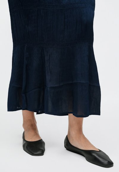 Tumesinine kihiline maksikleidi, millel on vertikaalsed voldid ja voolav ääris; sellele on lisatud mustad, madala kontsaga, ümarate otstega kingad, mis on valmistatud siledast nahast.