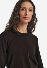 Czarny, miękki sweter z dzianiny z okrągłym dekoltem i długimi rękawami. Charakteryzuje się gładką fakturą i lekko dopasowanym krojem.