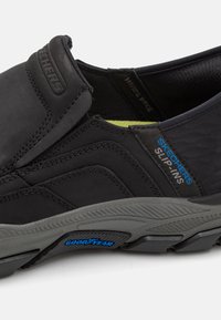 Skechers slip-on shoes in black with textured upper, elastic side panels, and gray rubber outsole featuring blue "Goodyear" logo detail.