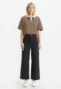 Gestreept bruinen en crèmekleurig poloshirt met een witte kraag, gecombineerd met high-waisted zwarte wijde jeans en witte sneakers.