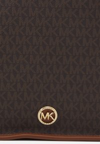 Mörkbrunt texturerat tyg med ett upprepat "MK" mönster och en rund guld "MK Michael Kors" logotyp nära nederkanten med detaljer av brunt läder.
