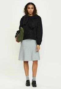 Must must have, mille pealmine, must helmega, hall volangseelik, oliivroheline kott, hall sokid, mustad mokassiinid, lokkis juuksed, neutraalne taust.