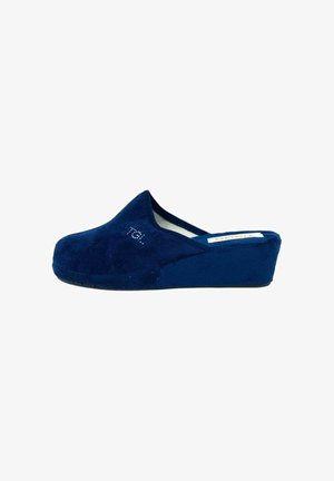 Zoccoli in suede blu navy con suola a zeppa. Presentano una punta chiusa, una texture morbida e un piccolo logo vicino al lato. Fodera interna liscia.
