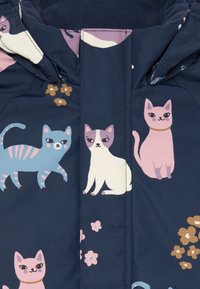 Giacca in tessuto navy con gatti illustrati colorati in varie posizioni, arricchiti da dettagli floreali. Texture liscia e design con chiusura a zip.