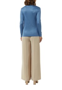 Langsleeve, glad blauwe top gecombineerd met losse, beige broek. Beide kledingstukken hebben een moderne snit met minimale details.