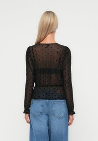 Zwarte transparante blouse met lange mouwen, stippenpatroon, relaxte pasvorm, gathered taille en ronde halslijn. Gekenmerkt met blauwe wijde spijkerbroeken.