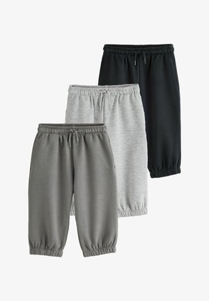 Trzy pary spodni dresowych z elastycznym pasem i ściągaczami na kostkach w kolorze czarnym, jasnoszarym i ciemnoszarym, ułożone nałożone na siebie na białym tle.