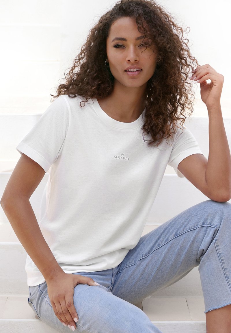 White cotton t-shirt with a round neck and short sleeves, featuring a small "Copenhagen" logo. Worn with light blue jeans.