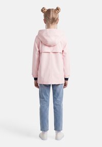 Παιδί που στέκεται με την πλάτη γυρισμένη, φορώντας ένα ανοιχτό ροζ μπουφάν με κουκούλα, ανοιχτό μπλε τζιν παντελόνι, λευκά αθλητικά παπούτσια και δύο κοτσίδες σε στυλ "διάστημα".